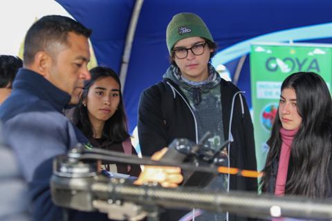 Un grupo de jóvenes observa atentamente una demostración de un dron en un evento al aire libre.
