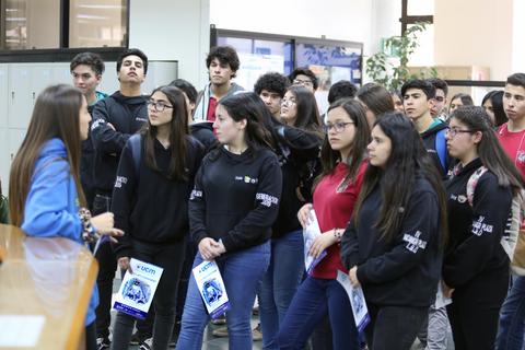 Un grupo de estudiantes escucha atentamente a una presentadora en un edificio educativo.