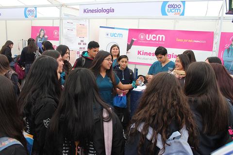 Un grupo de estudiantes visitan un stand de kinesiología en una feria educativa.