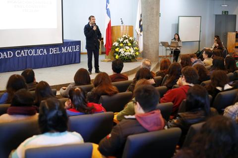 Una conferencia en la Universidad Católica del Maule con un ponente frente a una audiencia sentada.