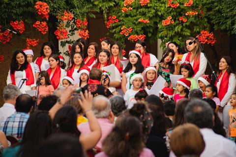 Un grupo de personas canta en un evento, rodeados de flores y decoraciones festivas.