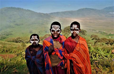 Tres niños sonrientes con pinturas faciales posan delante de un paisaje montañoso.