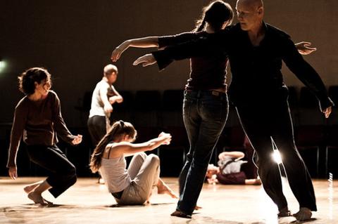 Un grupo de personas realiza una coreografía en un escenario con luz tenue.