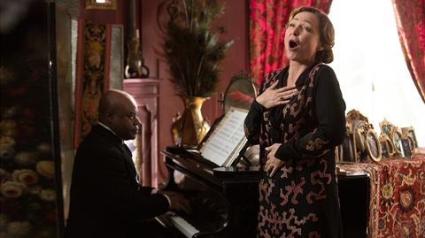 Una mujer canta apasionadamente mientras un hombre toca el piano a su lado en un ambiente elegante.