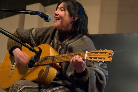 Una mujer canta y toca la guitarra mientras está sentada en un escenario.