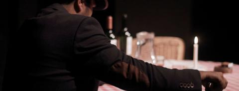 Un hombre sentado en una mesa con una vela encendida y botellas de vino de fondo.