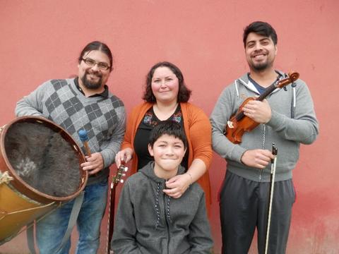 Un grupo de cuatro personas posando con instrumentos musicales frente a una pared de color rosa.