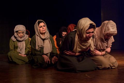 Un grupo de mujeres actuando en un escenario, mostrando emociones intensas y vistiéndose con ropa tradicional y pañuelos.