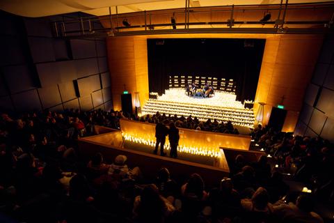 Una audiencia disfruta de un evento en un auditorio iluminado por velas.