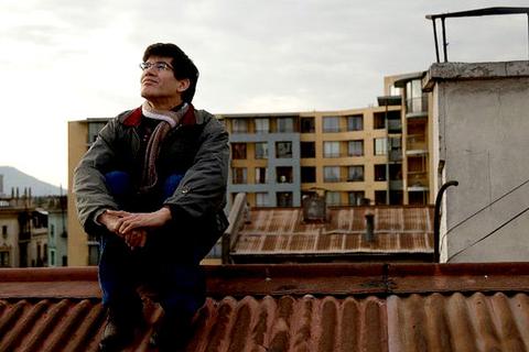 Una persona está sentada en el techo de un edificio, mirando pensativamente hacia el horizonte.