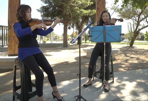 Dos violinistas interpretan música en un parque.