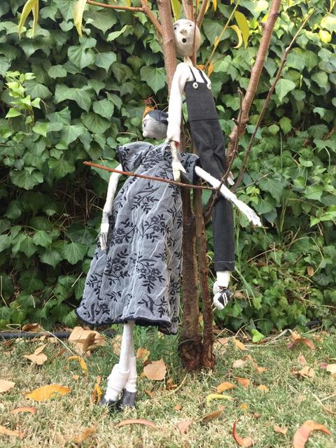 Dos figuras de muñecos de trapo sujetadas a un árbol en un entorno natural.