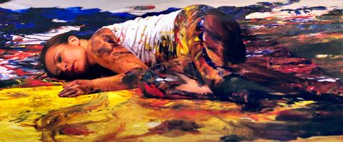 Una mujer está recostada sobre un fondo de pintura colorida, cubierta de pintura en su piel y ropa.