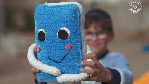 Un niño sostiene con alegría un muñeco azul de crochet con una sonrisa.