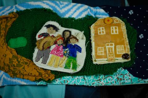 Una obra textil que representa una familia y una casa a través de figuras y bordados.