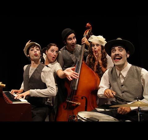 Un grupo de cinco músicos caracterizados con vestimenta vintage, posando de manera divertida en un escenario.