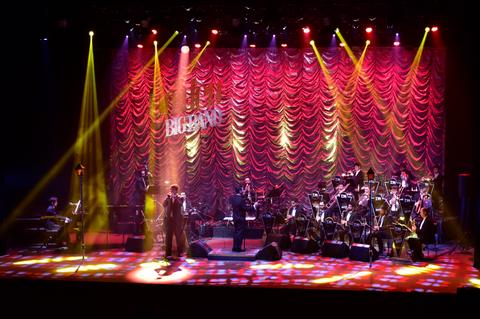 Un espectáculo musical en un escenario iluminado con una orquesta y un cantante.