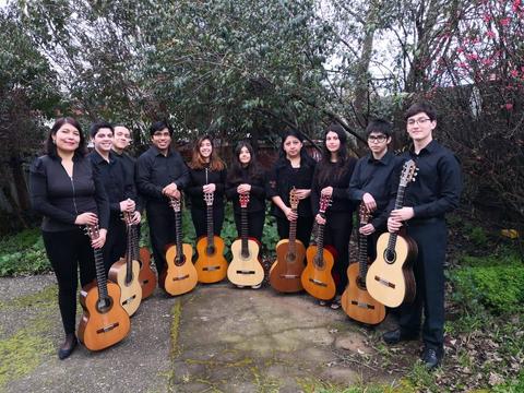 Un grupo de jóvenes músicos posando en un jardín, todos vestidos de negro y sosteniendo guitarras.