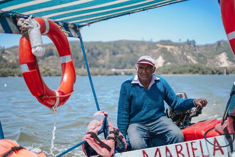 Un hombre mayor navega en un bote sobre un lago, con un salvavidas visible a su lado.