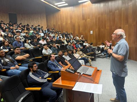 Un profesor está dando una charla a una audiencia llena de estudiantes en un auditorio.