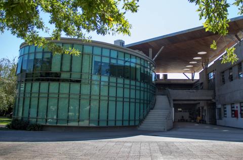Esta imagen muestra un edificio moderno con paredes de vidrio en un ambiente soleado.