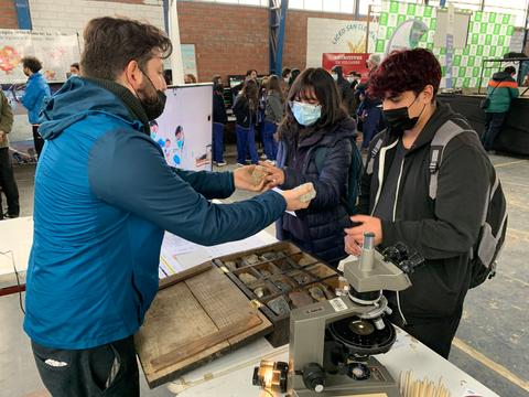 Un grupo de personas interactúa en un evento educativo donde se presentan experimentos científicos.