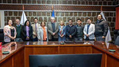 Un grupo de personas se encuentra en una sala de reuniones con banderas en el fondo.