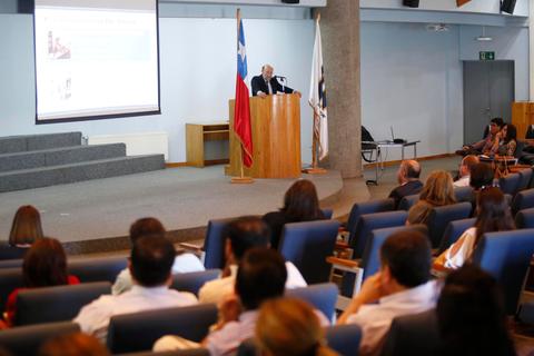 Una conferencia en un auditorio con un ponente frente a un público atento.