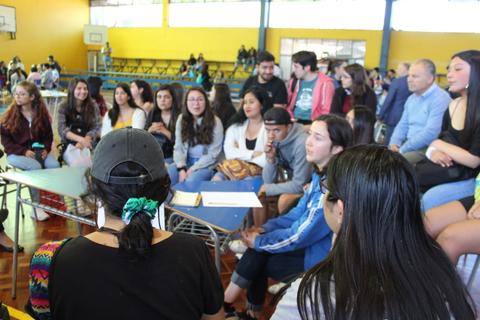 Un grupo de jóvenes sentados en un salón de clases interactuando entre sí.