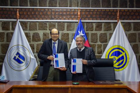 Dos hombres sostienen documentos en una ceremonia oficial con banderas chilenas de fondo.
