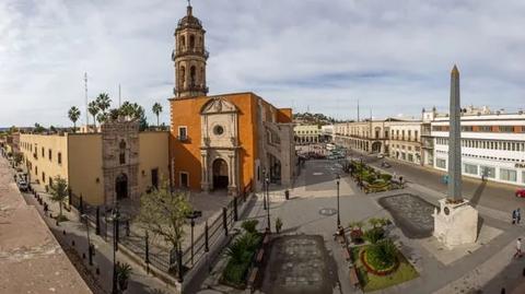 Vista panorámica de una plaza con edificios históricos y un obelisco en el centro.