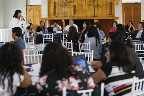 Una mujer presenta en una reunión con varias personas sentadas y escuchando atentamente.