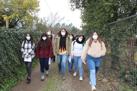 Un grupo de jóvenes camina por un sendero arbolado, llevando mascarillas y documentos en la mano.