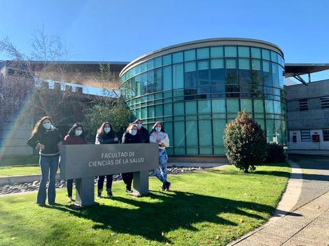 Grupo de personas posando frente a la Facultad de Ciencias de la Salud en un día soleado.