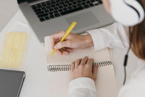 Una persona está tomando notas con un bolígrafo amarillo mientras escucha música usando auriculares.