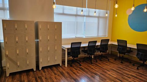 La imagen muestra un espacio de trabajo con taquillas grises y sillas negras.