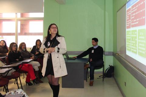 Una persona presenta en un aula frente a un grupo de asistentes que la observan atentamente.
