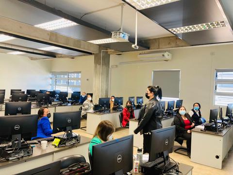 Una sala de computadoras con varias personas sentadas frente a pantallas en un ambiente educativo.