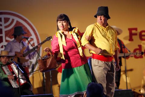 Una pareja de personas vestidas con trajes tradicionales de fiesta presenta un espectáculo musical en un evento cultural.