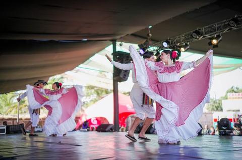 Un grupo de danzantes chilenos muestra un baile tradicional con trajes coloridos en un escenario al aire libre.