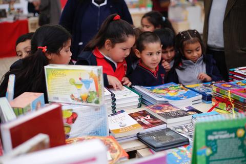Un grupo de niños observando una mesa llena de libros en un ambiente de feria.