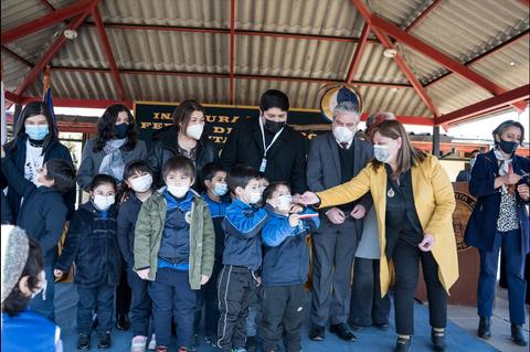 Un grupo de niños y adultos en un evento de inauguración al aire libre, todos usando mascarillas.