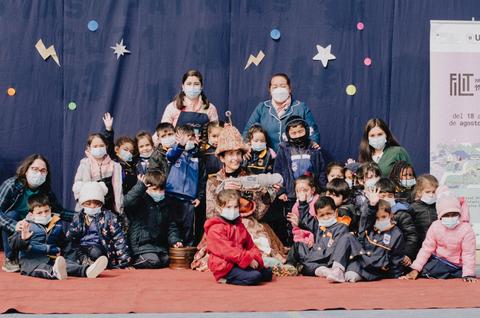 Un grupo de niños y adultos posan juntos en un evento, todos usando mascarillas y con un fondo decorado.