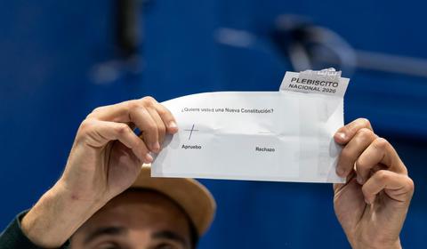 Una persona sostiene una boleta de plebiscito en la que se pregunta sobre una nueva constitución.