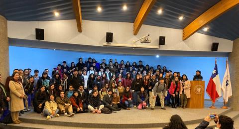 Un gran grupo de personas posando en un auditorio con una bandera chilena y un podio en el fondo.