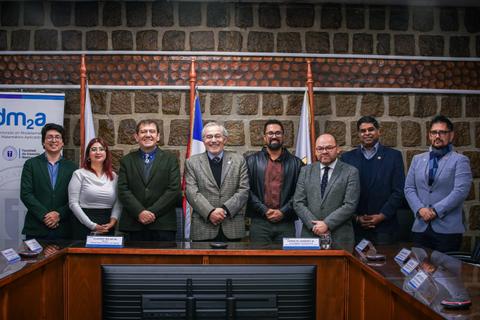 Un grupo de personas posando en una sala de reuniones con banderas de fondo.