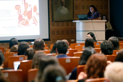 Una conferencista presenta un tema a un grupo de personas en una sala con asientos organizados.