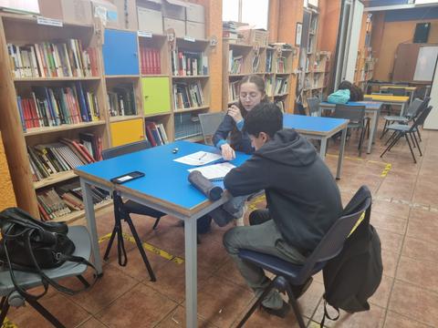Dos estudiantes conversan y estudian en una biblioteca.