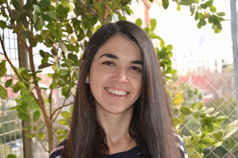 Una mujer sonriendo frente a una pared con plantas.