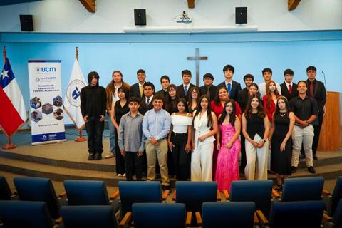 Grupo de estudiantes en ceremonia de graduación en un salón con banderas chilenas.